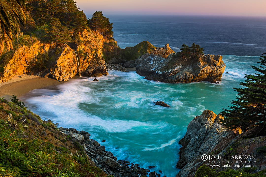 Fine art photograph of McWay Falls at sunset in Big Sur, California, featuring a lone palm tree and lush green foliage framing a turquoise cove where a waterfall spills onto the beach.