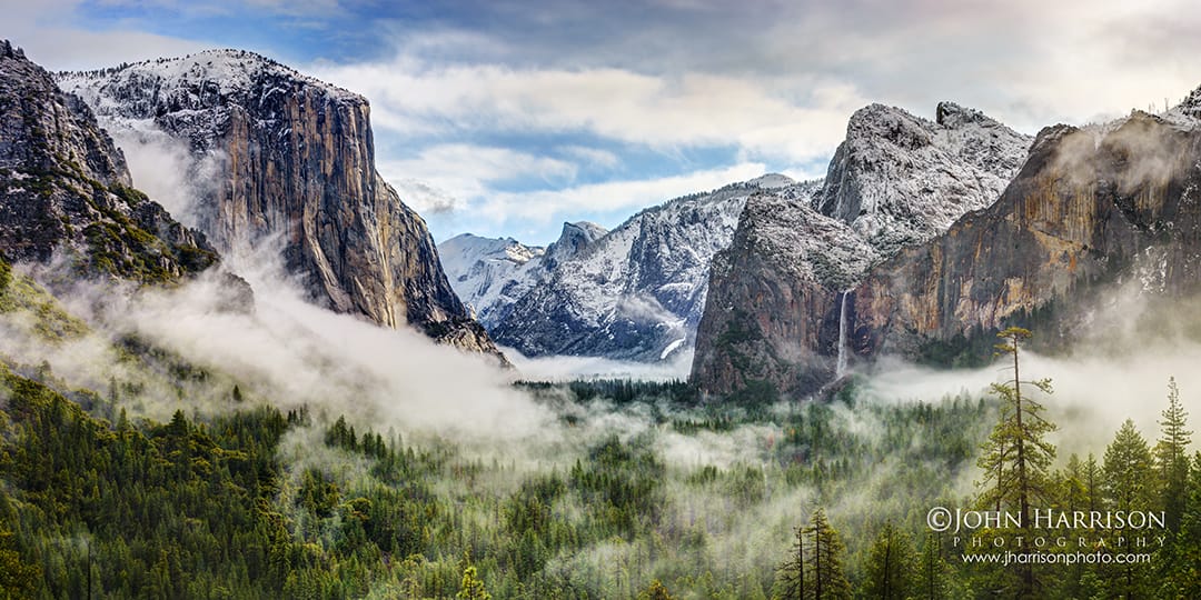 Winter view from Tunnel View overlooking Yosemite Valley with El Capitan, Bridalveil Fall, snow-covered granite cliffs, and morning fog drifting through the pine forest in Yosemite National Park, California.