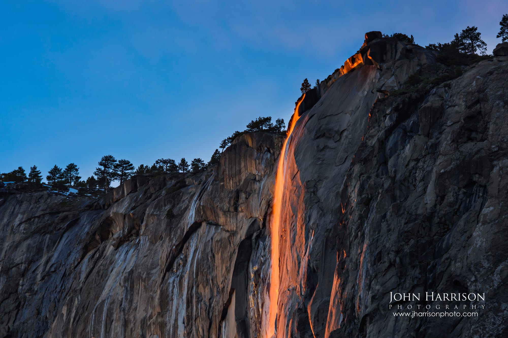 A horizontal fine art landscape photograph of the Yosemite Firefall at blue hour, showing a close-up view of the glowing orange Horsetail Falls against the dark, textured granite of El Capitan.