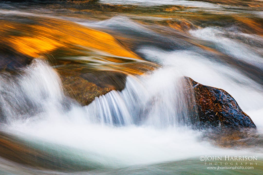 Long exposure abstract of the Merced River in Yosemite National Park, silky water flowing over granite rocks with golden sunset reflections, demonstrating creative water and texture photography.