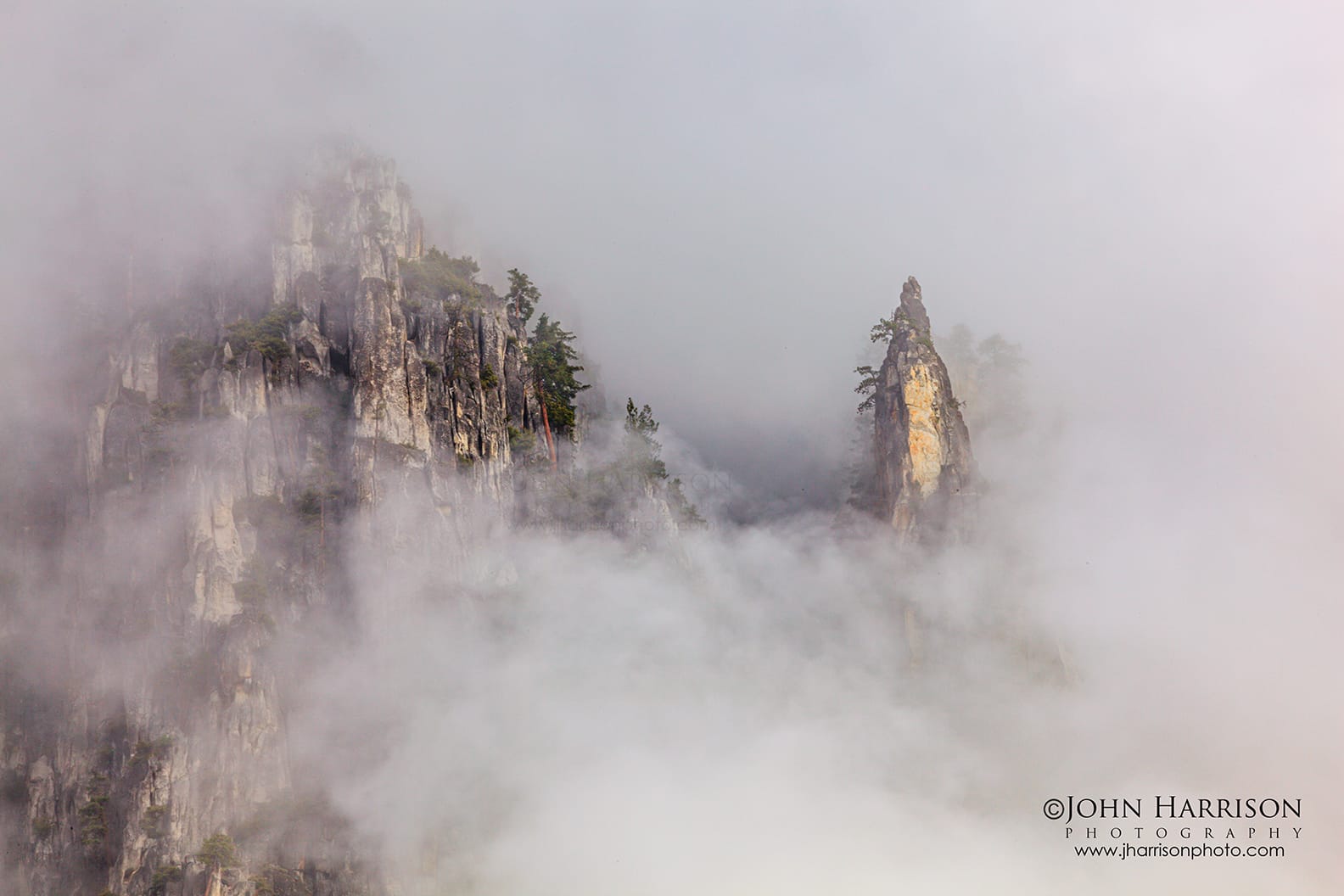 Granite spires rising through winter mist near Yosemite Falls in Yosemite National Park, with drifting fog and pine trees after a clearing storm.