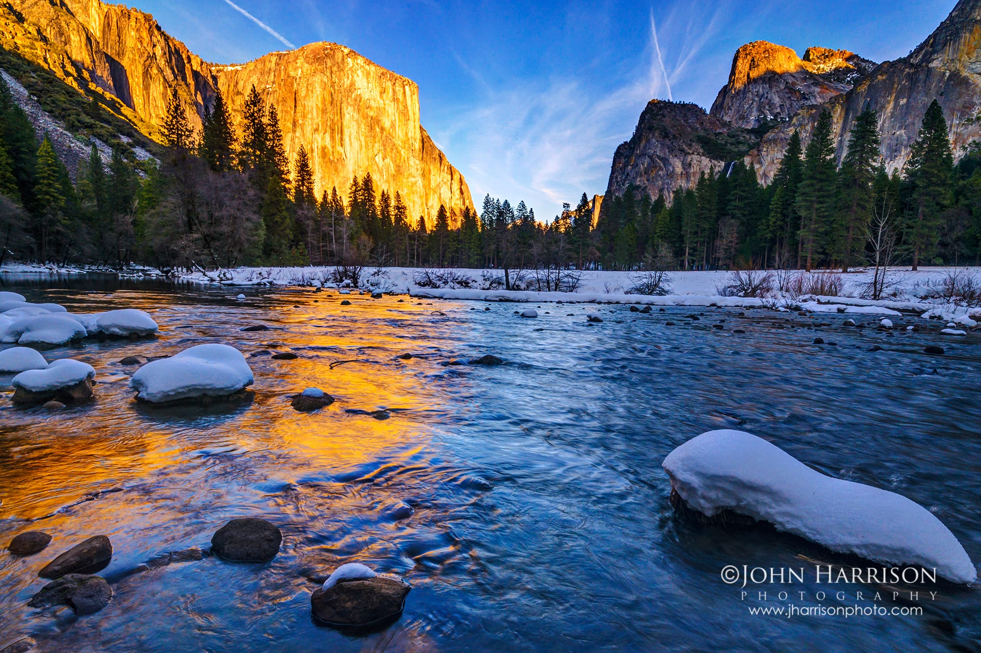 El Capitan glowing at sunset above the snow-covered Merced River in Yosemite Valley during winter, with golden light reflecting on flowing water.