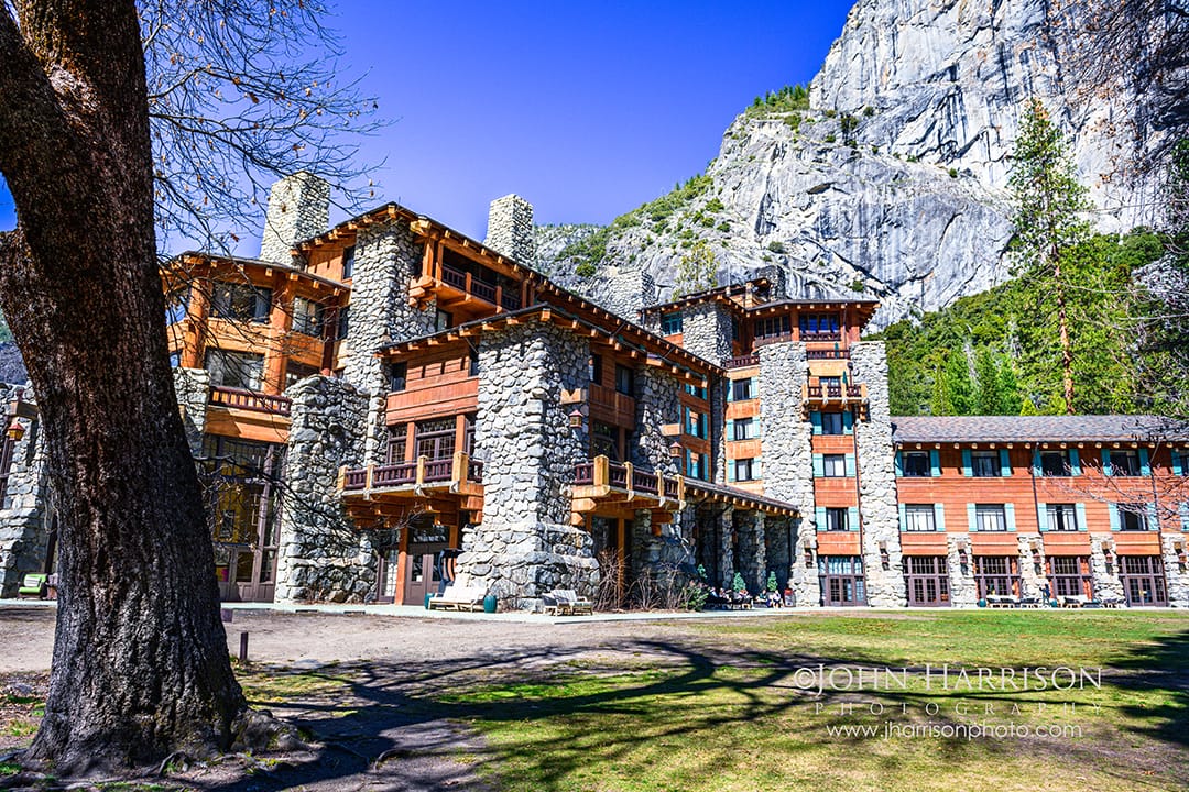 The Ahwahnee Hotel in Yosemite Valley with stone architecture, tall windows, and garden lawn beneath granite cliffs in Yosemite National Park.