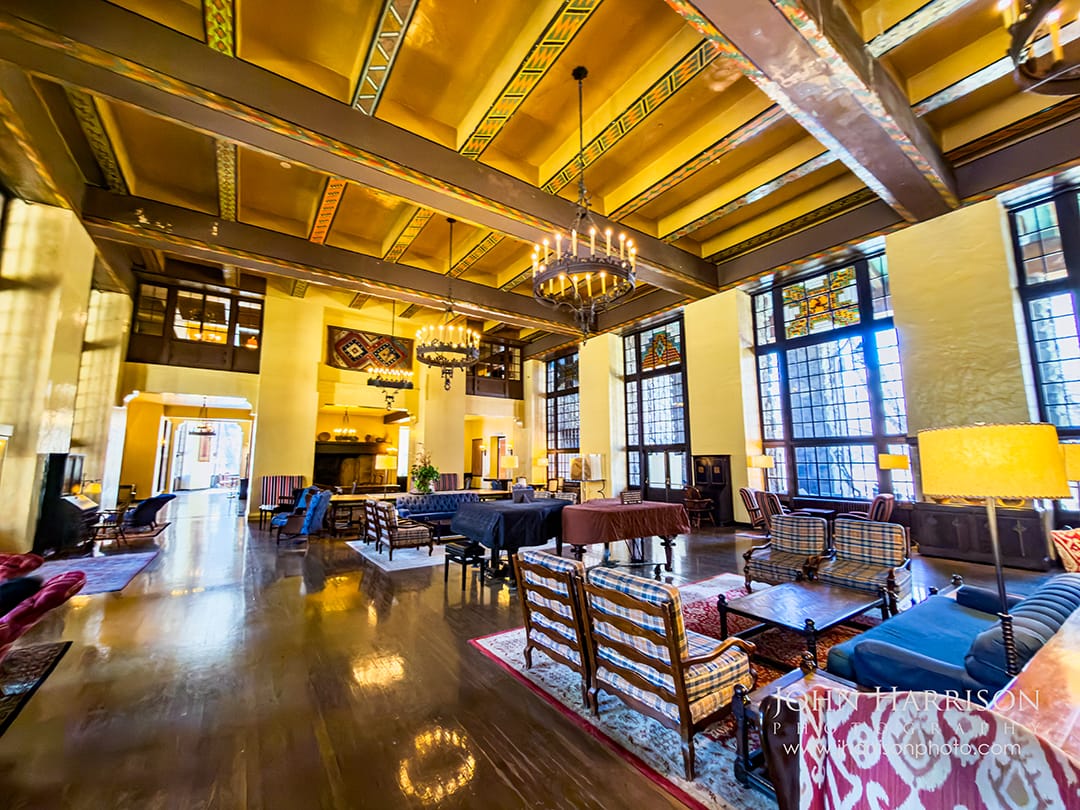 Lobby inside The Ahwahnee Hotel in Yosemite National Park with large stone fireplace, timber beams, chandeliers, and tall windows overlooking Yosemite Valley.