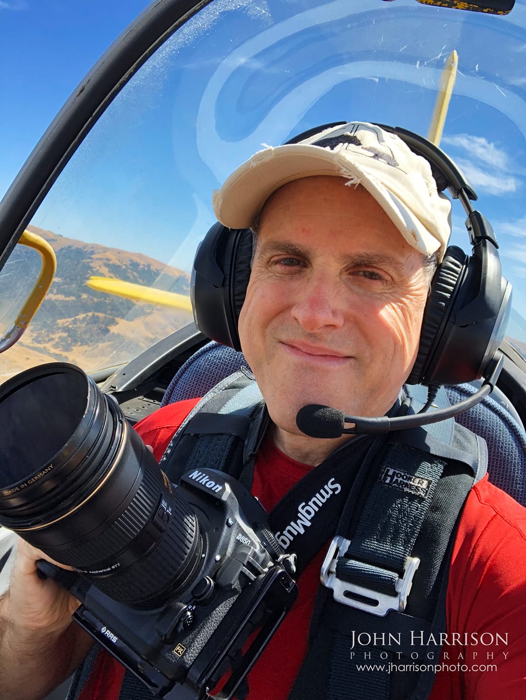 John Harrison landscape photographer flying in the backseat of a T-32 aircraft holding a Nikon D850 with SmugMug camera strap while capturing aerial photography over the San Francisco Bay Area, California.
