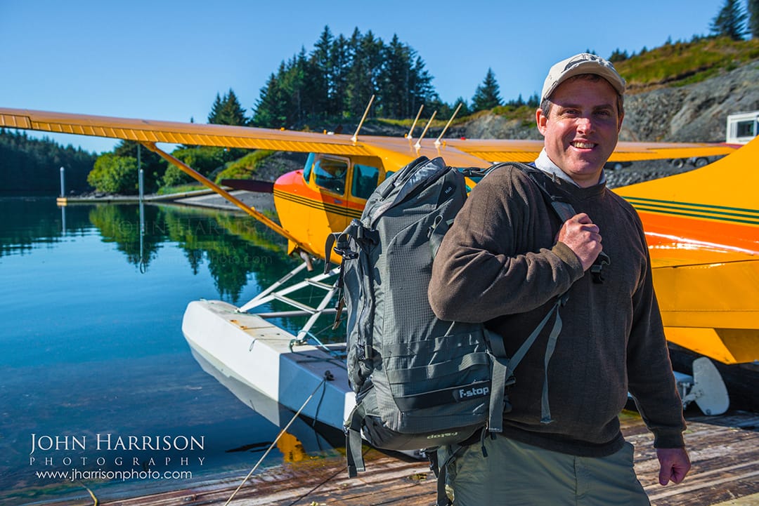 John Harrison nature and landscape photographer standing beside an Alaskan seaplane with his F-Stop Tilopa backpack and Nikon camera gear before departing for Katmai National Park and Preserve Alaska for wildlife photography.