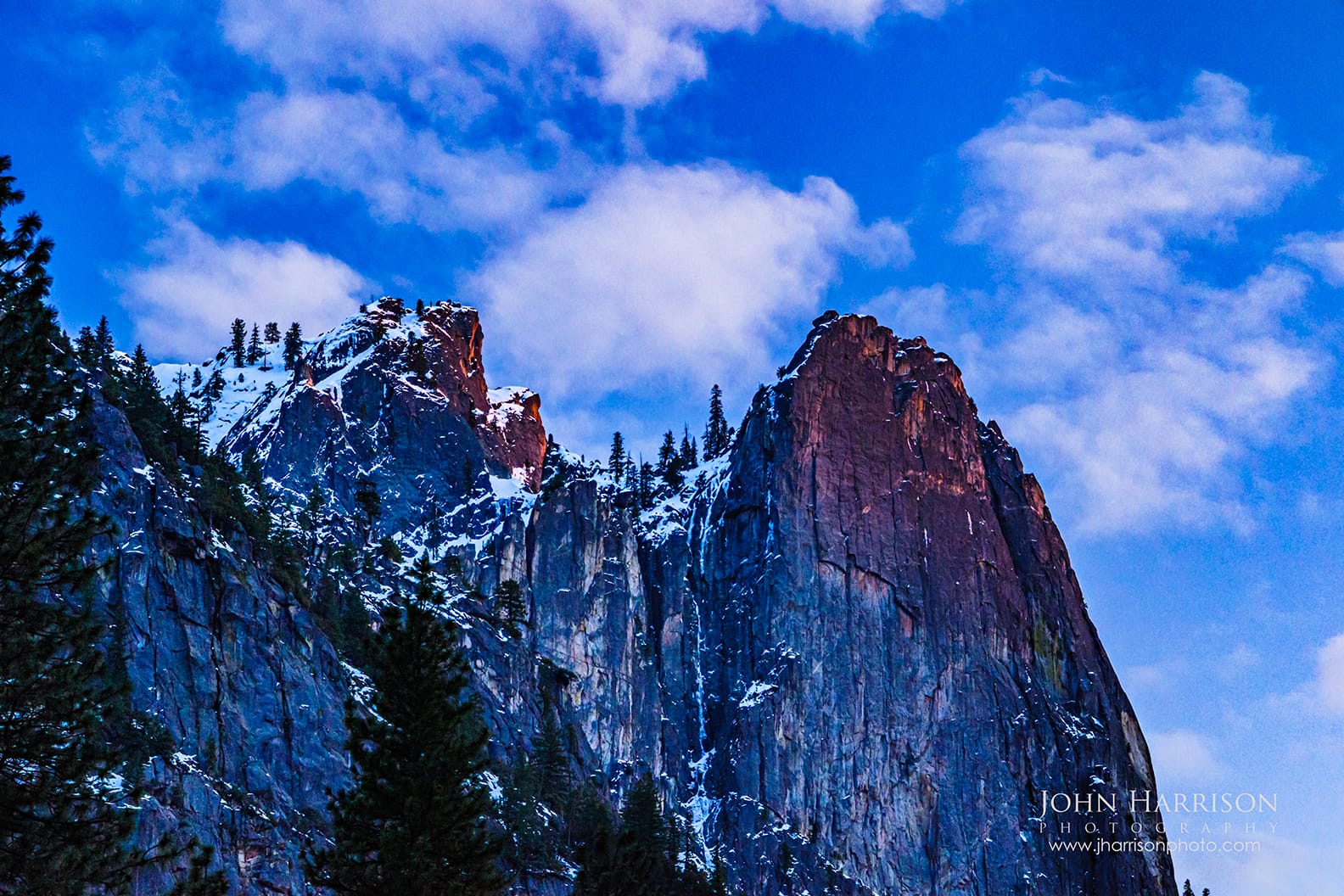 Sentinel Rock glowing with spring alpenglow during blue hour in Yosemite Valley with snow on granite cliffs and clouds above Yosemite National Park.