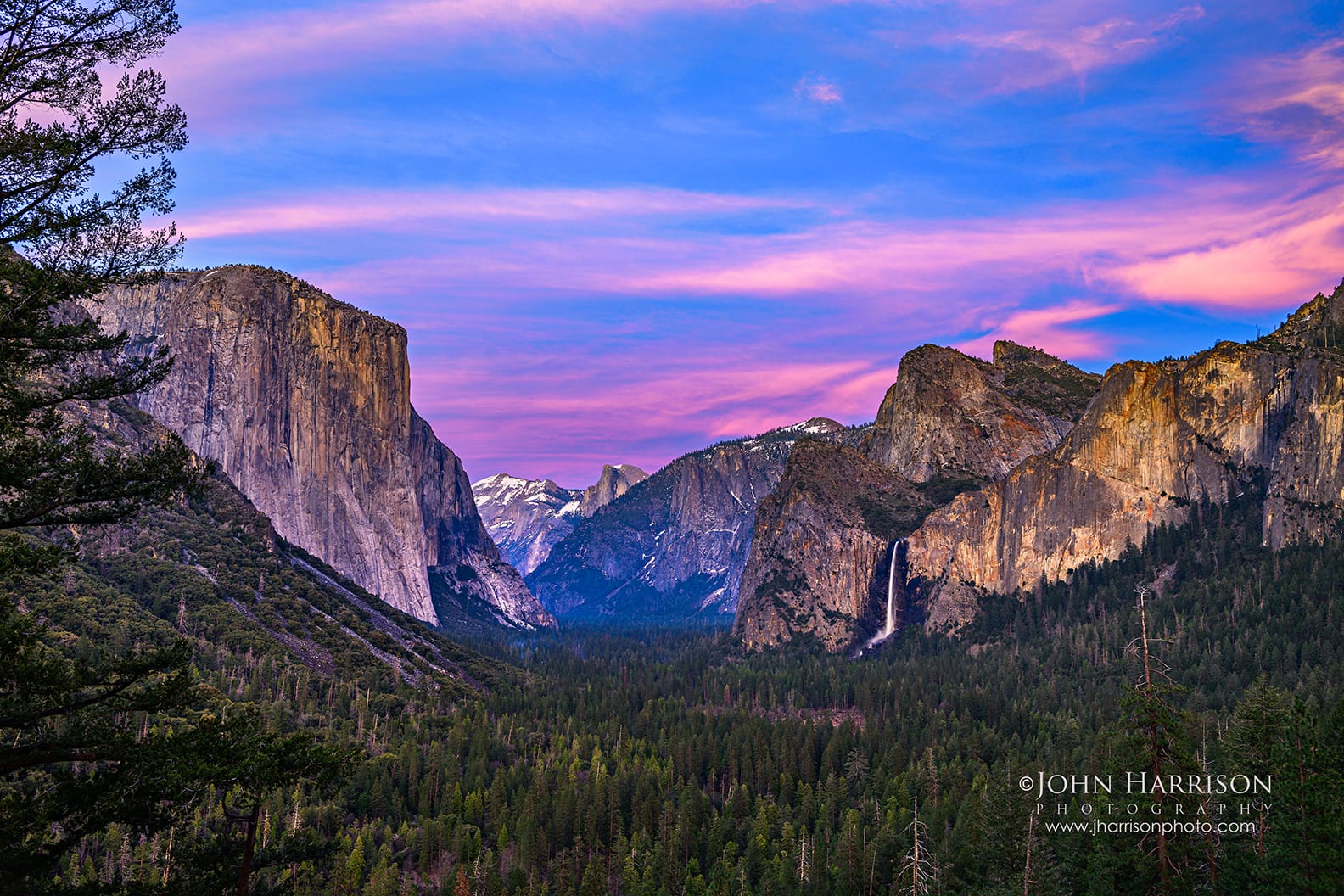 Twilight sky glowing above Yosemite Valley from Tunnel View with El Capitan and Bridalveil Fall beneath colorful spring clouds in Yosemite National Park, California.