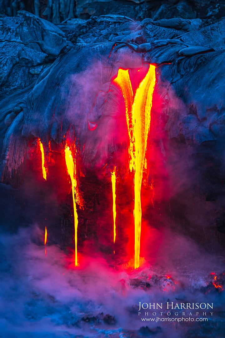 Lava flowing into the Pacific Ocean at Hawaii Volcanoes National Park on the Big Island as glowing molten rock drips over a coastal cliff and steam rises where the lava meets the sea.