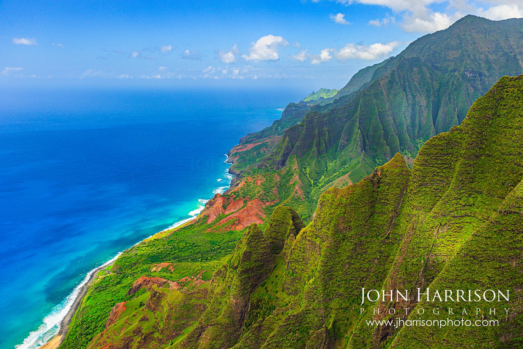 Aerial view of the dramatic green cliffs of the Nā Pali Coast on Kauai, Hawaii with red volcanic ridges and deep blue Pacific Ocean captured from a helicopter