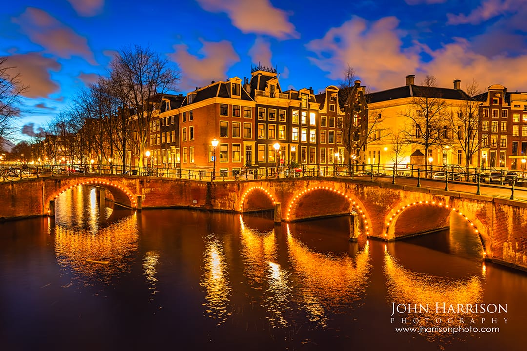 Illuminated canal bridges reflecting on the water at blue hour, Amsterdam Canal Ring, Netherlands