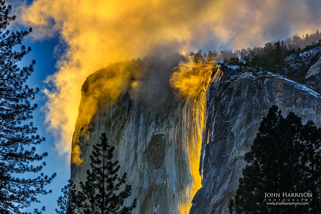 Yosemite Firefall at Horsetail Fall glowing gold at sunset on El Capitan, with dramatic clouds and pine silhouettes in Yosemite National Park during winter.
