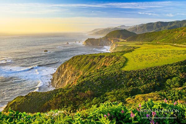 Fine art landscape photograph of Bixby Bridge in Big Sur, California, featuring rugged rocky hillsides, vibrant green foreground grasses, and the Pacific coastline 